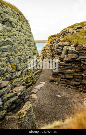 Die Außenmauer der Brosche, ein in Schottland einzigartiger Turm aus der Eisenzeit, links und das Pictish-Steuerhaus rechts darüber in Jarlshof, Stockfoto