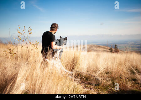 Mann mit schwarzen und weißen Border Collie sitzend in hohen goldenen Gras auf der Bergwiese. Auf den Hund konzentrieren. Stockfoto