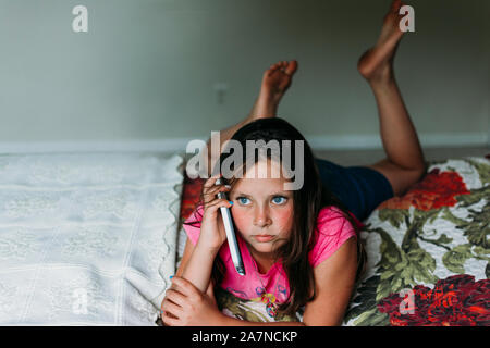 Tween Girl Festlegung auf ein Bett mit einem Mobiltelefon Stockfoto