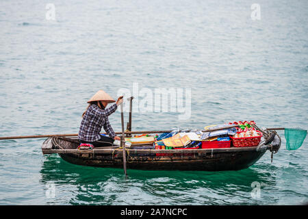 Ha Long Bay, Vietnam - 15. Oktober 2019: Eine lokale Frau Zeilen bis zu Kreuzfahrtschiffen und Junk-Boote mit billig essen und Bier Stockfoto