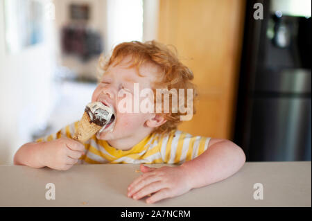 Kleinkind einen grossen Bissen von seinem Eis kommen zu Hause in der Küche Stockfoto