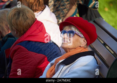 Charkow, Ukraine - Oktober 14, 2019: Elegante ältere Dame in einem roten Barett auf einer Bank in einem Park Stockfoto