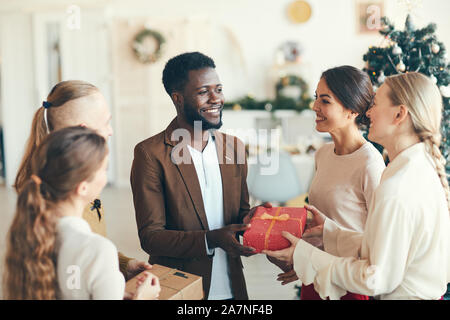 Multi-ethnischen Gruppe von fröhlichen jungen Menschen den Austausch von präsentiert während der Weihnachtsfeier in gemütlicher Atmosphäre, kopieren Raum Stockfoto