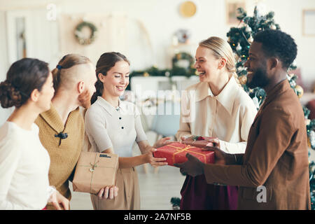 Taille bis Portrait von fröhlichen jungen Menschen den Austausch von präsentiert während der Weihnachtsfeier in gemütlicher Atmosphäre, kopieren Raum Stockfoto
