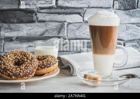 Konzeptionelle süßen Frühstück. Latte macchiato Kaffee mit süßen Krapfen mit einem Loch und Tageszeitung. Stockfoto