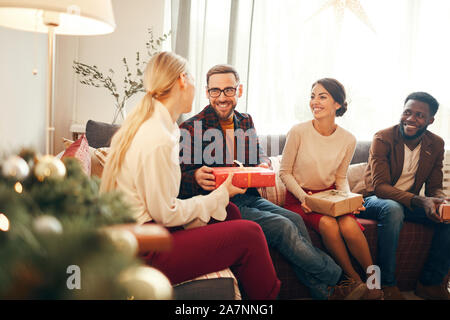 Gruppe von eleganten Erwachsenen Austausch präsentiert auf Weihnachten, auf bärtiger Mann lächelt glücklich halten roten Geschenkkarton, kopieren Raum konzentrieren Stockfoto