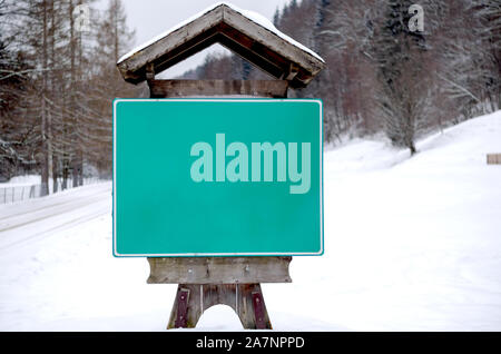 Straßenschild hängend auf einer Holzplatte, die die Form eines Hauses bei der Ausfahrt aus einem Bergdorf hat im Winter. Stockfoto