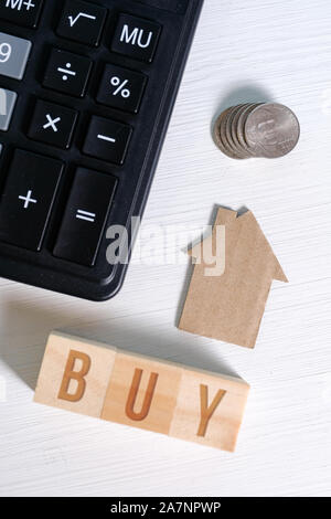 Abstrakte Pappe Haus neben einen Taschenrechner und Münzen, das Wort kaufen. Das Konzept für die Berechnung der Kosten des Gehäuses. Vertikale. Stockfoto