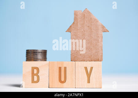 Abstrakte Pappe Haus neben Münzen, das Wort kaufen auf Würfel. Das Konzept der Akkumulation von Geld für den Wohnungsbau. Close Up. Stockfoto