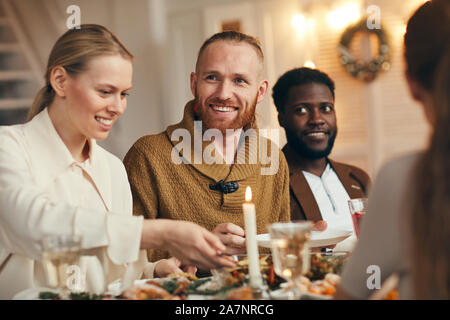 Porträt des zeitgenössischen bärtiger Mann lächelt glücklich, während wir Weihnachten feiern mit Freunden und Familie am Tisch Stockfoto