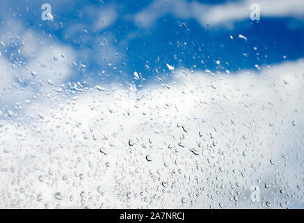 Regentropfen auf dem transparenten Fenster Glas gegen bewölkt blauer Himmel, während der Regenzeit. Stockfoto