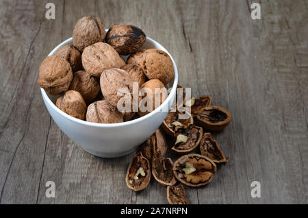 Stapel der ganzen und gebrochenen Walnüsse in eine weiße Keramik Schüssel auf dem Tisch. Stockfoto