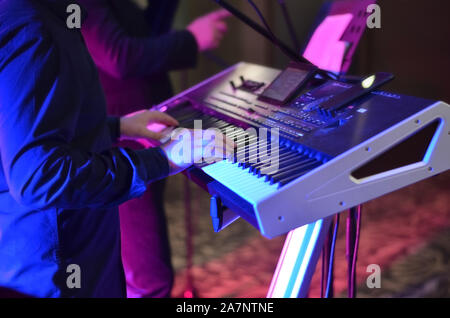 Mann Singen in einem elektronischen Synthesizer auf einer Party in der Nacht mit blauem Licht im Hintergrund. Stockfoto