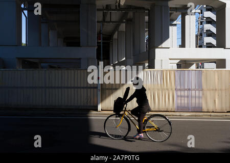 Eine Frau fährt mit dem Fahrrad unter einer Überführung auf den Schienen der Keio-Linie in der Nähe von Kichijoji, Tokio, Japan. Stockfoto