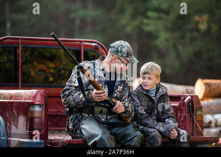 An seinem Fahrzeug mit seinem Sohn in den Wald. Jäger lehrt junge Junge, wie Sie mit der Schrotflinte Gewehr Stockfoto