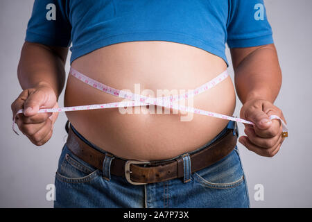 Übergewicht oder Fett erwachsenen Mann in sehr engen Jeans mit Maßband auf grauem Hintergrund. Gesundheitswesen, Medizin Konzept. Stockfoto