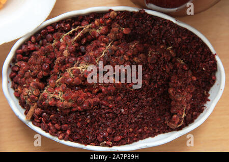 Getrocknete sumac Gewürz in eine hölzerne Schüssel, Ansicht von oben. eine Handvoll roter Sumach Pulver in einer Platte abstrakt Hintergrund. Sumak Körner und Pulver. Sumac ist in Stockfoto