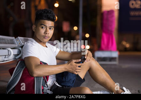 Junge asiatischer Mann denken, während Sie das Telefon in den Straßen der Stadt bei Nacht Stockfoto