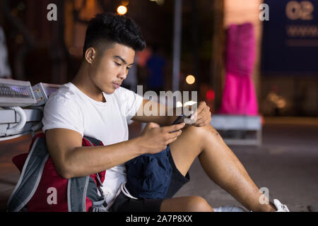 Junge asiatischer Mann mit Phone in den Straßen der Stadt bei Nacht Stockfoto