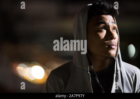 Gesicht der jungen asiatischen Mann mit Kapuze Denken in den Straßen der Stadt bei Nacht Stockfoto