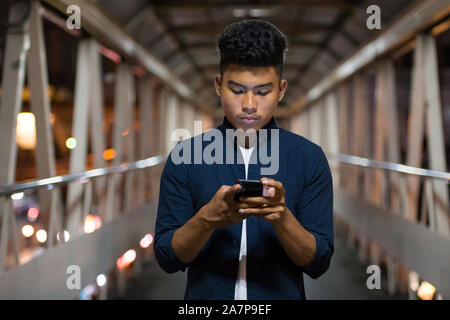 Junge asiatischer Mann können Sie über das Telefon auf die Fußgängerbrücke bei Nacht Stockfoto