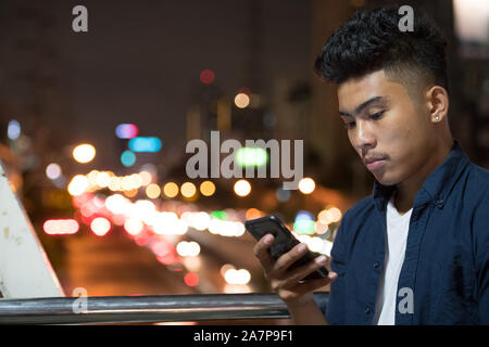 Gesicht der jungen asiatischen Mann mit Telefon vor der Blick auf die Straßen der Stadt bei Nacht Stockfoto