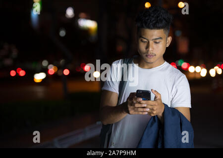 Junge asiatischer Mann mit Phone in den Straßen der Stadt bei Nacht Stockfoto