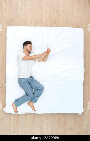 Bedtime. Guy liegend auf Bett Draufsicht unter selfie auf dem Smartphone heiter Stockfoto
