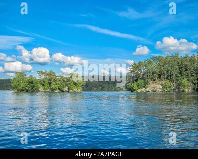 Einen sonnigen Tag auf einer kanadischen See im Sommer, mit einem Boot von zwei bewaldeten Inseln. See Memphremagog, Quebec. Stockfoto