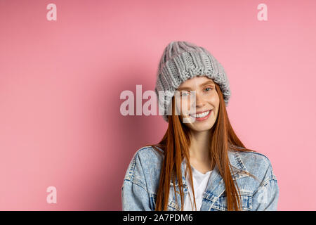Wunderschöne kaukasischen Ingwer sommersprossiges Mädchen Student ohne Make-up in Trendy Strickmütze, Jeans Jacke an Kamera suchen mit fröhlich-Ausdruck über p Stockfoto