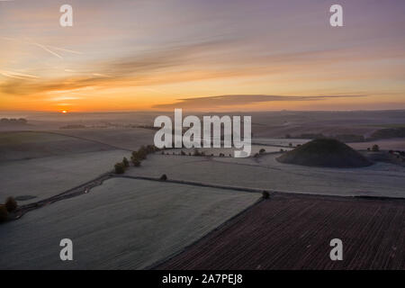 Silbury Hill, Nr Avebury, Wiltshire, UK. 28. Oktober 2019. Drone Bild von einem frostigen Roten morgen Himmel über dem alten künstlichen Erdhügel Silbury Hill. Stockfoto