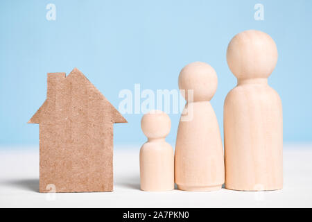 Holzfiguren Familie mit Karton ausschnitt Haus auf blauem Hintergrund. Konzept der Umzug zum neuen Haus, Siedlung, Miete, Hypotheken, Vertreibung. Stockfoto