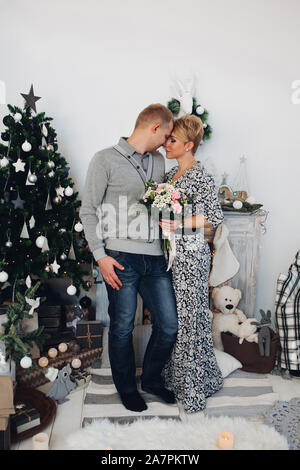 Schönes Paar mit Blumenstrauß am Weihnachtsbaum. Stockfoto