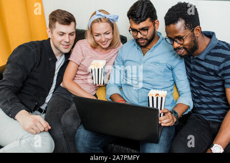 Gruppe von Freunden genießt die Zeit zusammen und suchen am Laptop. Multirassischen junge Menschen im Wohnzimmer zu Hause sitzen, Videos, po Essen Stockfoto