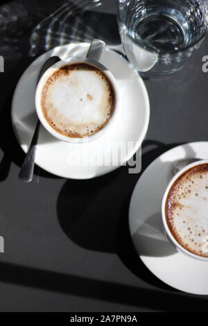 Frisch Gebrühter Cappuccino in Demitasse Cups mit Glas Wasser. Kaffee Trinken. Stockfoto