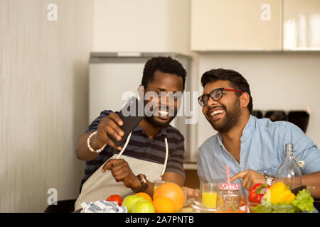 Zwei multirassischen Freunde Studenten am Tisch sitzen unter selfie zusammen, während der Vorbereitung Gemüsesalat und Fruchtsaft in der Herberge. Afrikanische Kerl mit i Stockfoto
