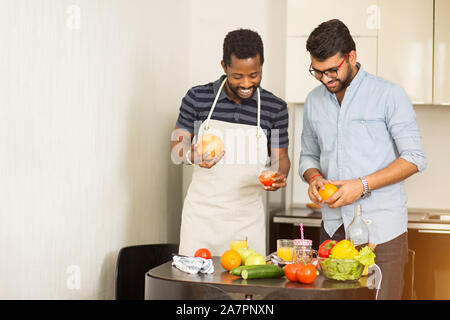 Schuß von zwei männlichen Freunden in Freizeitkleidung in der Küche. Junge Inder und seinem afrikanischen Freund trug Schürze Spaß beim Kochen Abendessen zusammen Stockfoto