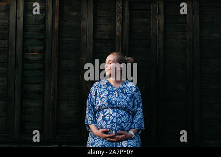 Portrait von schöne schwangere Frau. Sie steht in der Mitte der Straße und halten die Hände auf ihren Bauch. Stockfoto