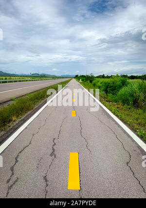 Perspektive Risse im Asphalt Weg auf den Berg. Lange Gerade beschädigt asphaltierte Straße. Schlechte Oberfläche der Radweg und weißen Himmel und Wolken mit Stockfoto