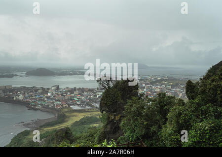 Üppiges Grün und Bäume auf Seongsan Ilchulbong auf düsteren Tag mit Stadt- und Meerblick Stockfoto