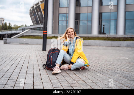 Schöne Mädchen, die von Telefon und sitzt auf Skateboard. Stockfoto