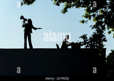 Silhouette einer Frau im Gespräch durch ein Megaphon vom Dach eines Gebäudes mit schönen blauen Himmel im Hintergrund Stockfoto