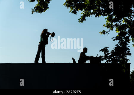 Silhouette einer Frau im Gespräch durch ein Megaphon vom Dach eines Gebäudes mit schönen blauen Himmel im Hintergrund Stockfoto