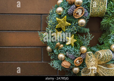 Handgefertigte Weihnachten Kranz aus frischem Tanne Baum mit goldenen Ornamenten Sterne flitter Walnüsse Band hängend auf Braun brick House Wand dekoriert. Stockfoto