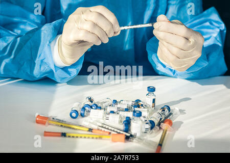 Arzt in einem blau OP-Kittel und Maske hält in seiner Hand ein medizinische Spritze und Flasche mit Insulin für Diabetes. Viele Spritzen und Medikamente für injectio Stockfoto