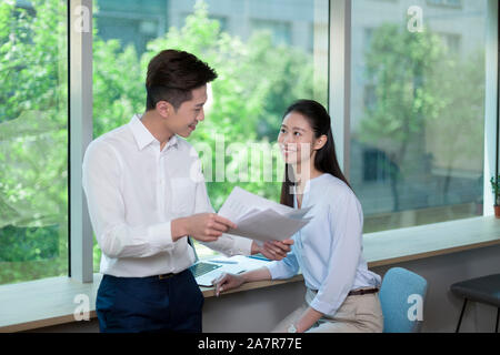 Taille, geschossen von zwei lächelnde männlichen und weiblichen Geschäftsleuten mit schwarzem Haar über Dokumente in einem Büro Stockfoto