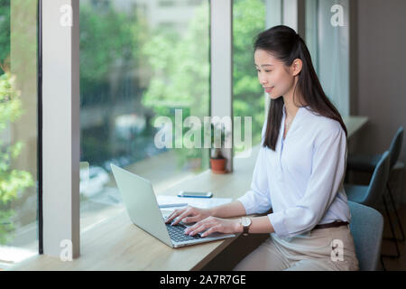 Seitenansicht Taille bis Schoß der jungen Geschäftsfrau mit geraden lange schwarze Haare mit einem Laptop an einem Schreibtisch in einem Büro Stockfoto