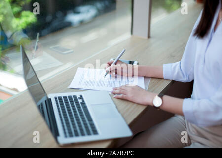 Midsection Schuß einer geschäftsfrau Schreiben in einem Dokument während an einem Schreibtisch mit einem Laptop im Büro sitzen Stockfoto