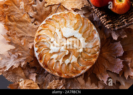 Frisch gebackene hausgemachten Apfelkuchen in der Nähe von roten Äpfel im Stroh Korb auf gelben Blätter im Herbst Hintergrund. Im rustikalen Stil Stockfoto