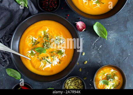 Kürbis und Karotten Suppe mit Sahne und Basilikum auf dunklem Hintergrund. Ansicht von oben mit der Kopie. Stockfoto